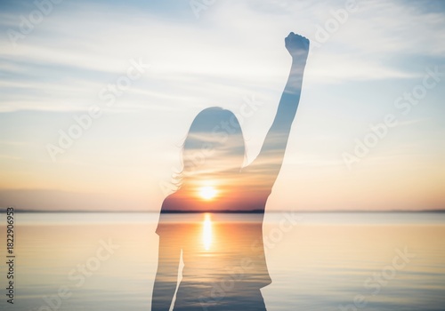 Empowered silhouette of a person with raised fist at sunset over water