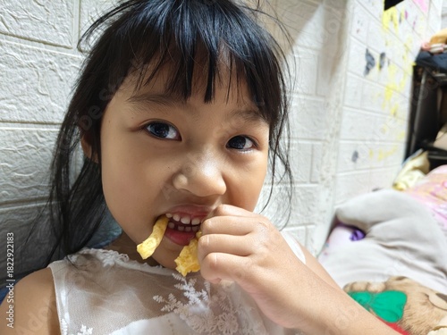 portrait of little asian girl eating snack , kid funny eat 