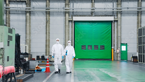 防護服を着て工場の中を歩く男女作業員
