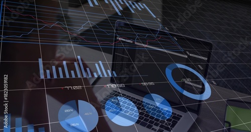 Displaying centered laptop showing blue charts at office desk, with keyboard, phone, green notebook