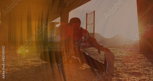 Stretching midadult man wearing dark hoodie and striped pants beneath overpass, holding sneaker