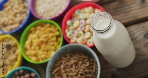 Displaying clear glass milk bottle with open neck on wood table, featuring cereal bowls, copy space