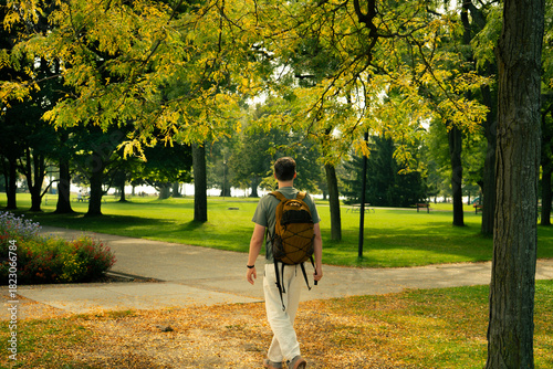 Photography A man with a backpack walks along a path in a lush green park setting