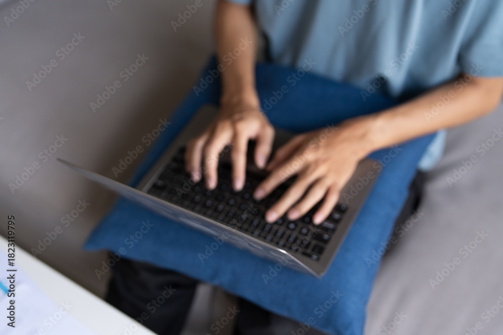 Fototapeta premium Asian Man Working from Home on Laptop with Technology Concept, Sitting on Sofa for Online Business and Remote Work Meeting