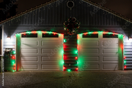 Garage doors are decorated with Christmas garlands, red ribbons, balls and a wreath at night