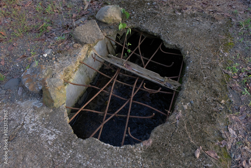 A damaged section of a road showing a large hole with exposed rusty rebar and broken concrete, posing a hazard to pedestrians and vehicles.