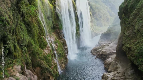 Aerial drone view of Tamul Waterfall cascading down green cliffs into a turquoise pool below