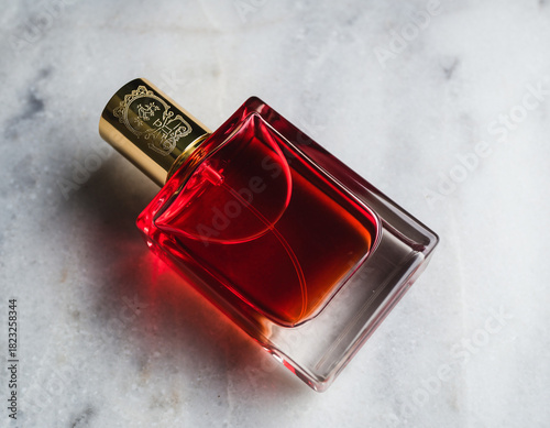 Perfume bottle filled with red liquid resting on marble surface reflecting light creating elegant and luxurious atmosphere.