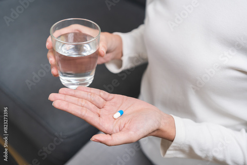 Sick, asian young woman, girl hand holding pill capsule, painkiller medicine from stomach pain, head ache, pain for treatment, take drug or vitamin and glass of water at home, pharmacy and health care