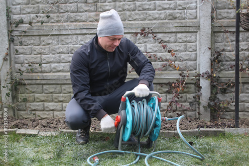 Men's chores, men's daily work tasks. A man coils a water hose before winter.