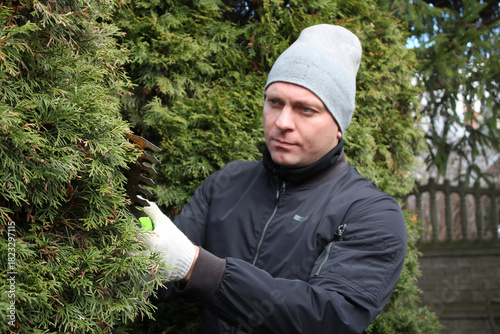 Men's chores, men's daily work tasks. A man in the yard trims a thuja with an electric trimmer.