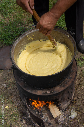 a person stirring a large batch of mămăligă, a traditional Romanian dish made from yellow maize flour. ,balmos