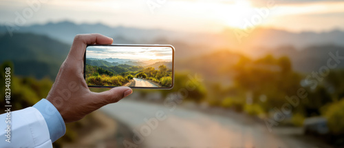 Wallpaper Mural Person holds smartphone capturing scenic view of winding road through lush green hills at sunset, creating serene and picturesque moment Torontodigital.ca