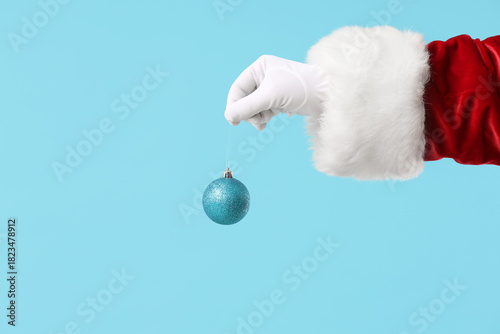 Santa Claus holding shiny Christmas ball on color background, closeup