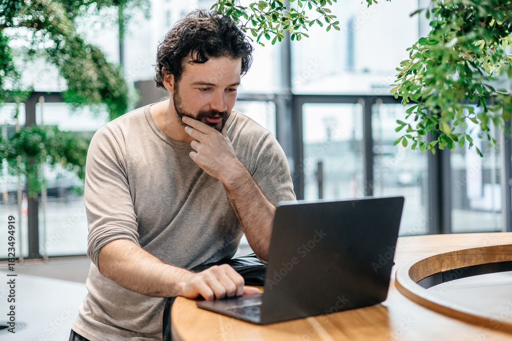 Ταπετσαρία Man concentrating on his laptop in a bright, plant-filled workspace