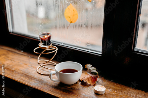 A warm mug of black tea by a rain-covered window, candlelight adding gentle cozy tones.