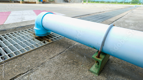 Roadside drainage channel with a steel grate cover and a large PVC pipe connected from the roof for effective rainwater discharge,