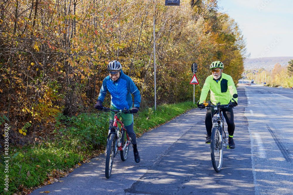 Fototapeta premium An old man who is passionate about cycling rides his bike with his son, enjoying a beautiful autumn day.