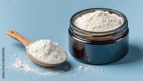 An open glass jar of creatine monohydrate powder and a wooden measuring spoon on a blue background. A sports supplement for training and muscle building.