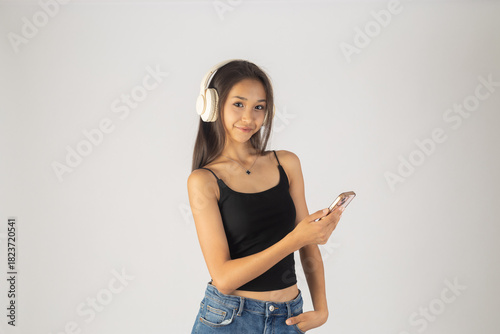 A woman wearing headphones is holding a smartphone and pointing at its screen