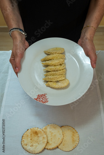 A person holding a porcelain plate containing homemade pasta called culurgiones