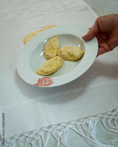 A person holding a porcelain plate containing homemade pasta called culurgiones
