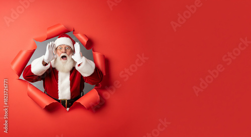 humorous photograph featuring Santa Claus popping out of a circular hole torn into a bright red background.