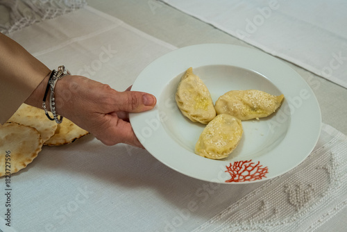A person holding a porcelain plate containing homemade pasta called culurgiones