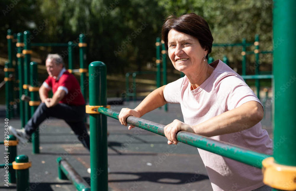 Fototapeta premium Mature woman doing push-ups from the crossbar on outdoor sports ground