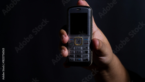 Wallpaper Mural Front view of a vintage mobile phone held in a hand against a dark studio background, showcasing its keypad and small screen. Ideal for illustrating obsolete tech or messaging Torontodigital.ca