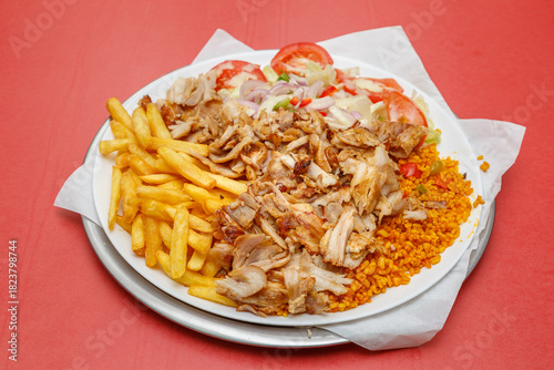 Assiette Döner Kebab avec frites, salade, blé dur sur fond rouge, restauration rapide, halal. 