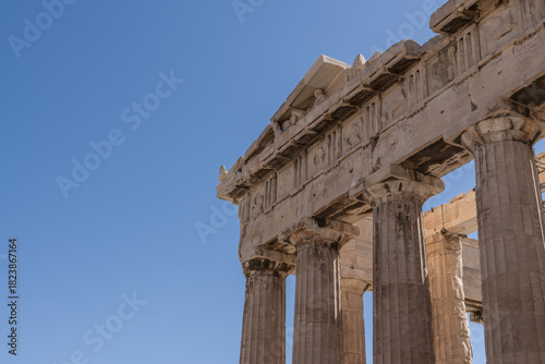 Detailed view of Parthenon frieze and corner columns in Athens. Detailed perspective of the Parthenon's corner showing carved friezes and robust Doric columns under bright sunlight.