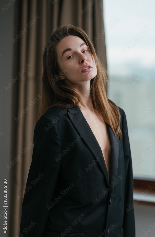 Fototapeta premium Portrait of a confident woman in a stylish, open blazer captured indoors with natural light streaming through the window