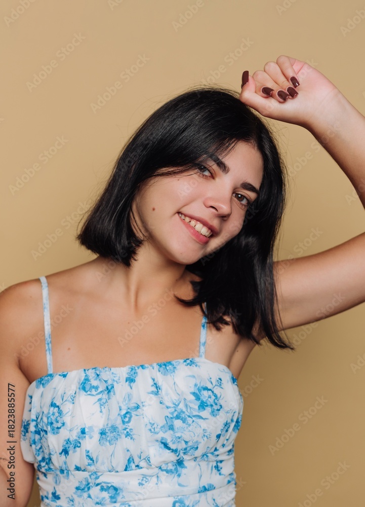 Fototapeta premium Smiling young woman in floral dress with cheerful expression against a plain yellow background