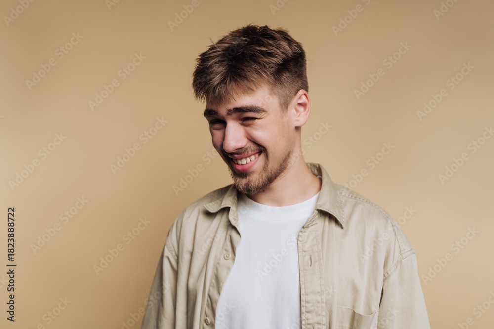 Obraz premium Joyful young man smiling in a light-colored shirt against a neutral background