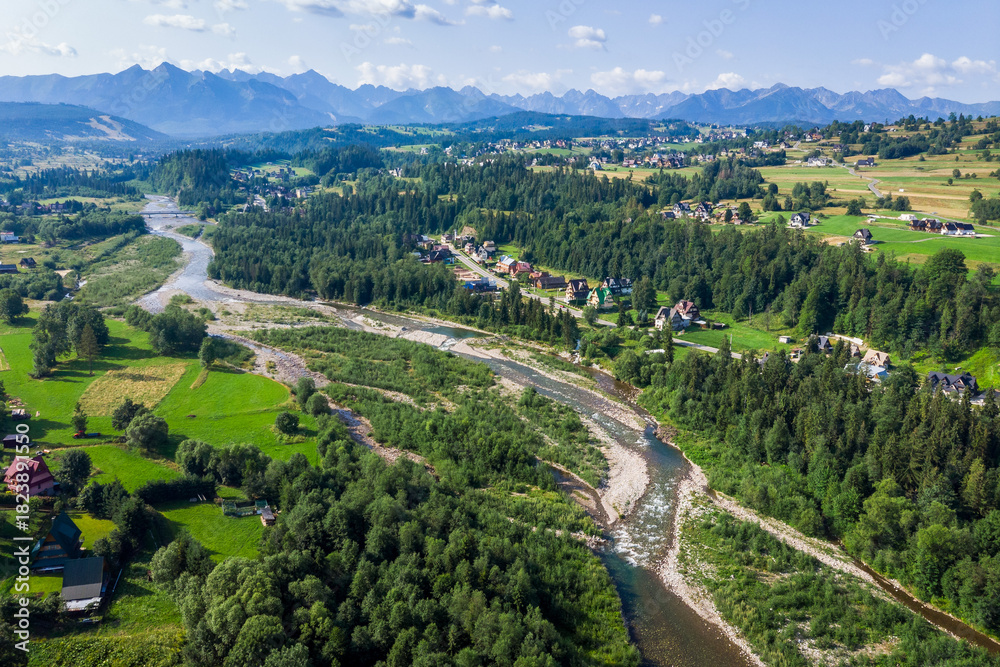 Obraz premium Wide aerial drone view of the Tatra Mountains and Białka Tatrzańska village. The braided Białka River flows through the valley, surrounded by green fields in July.