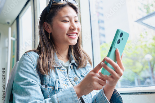 Excited woman looking at smartphone screen while traveling on public transport. Happy young female reading good news or message online, symbolizing communication, connection, success
