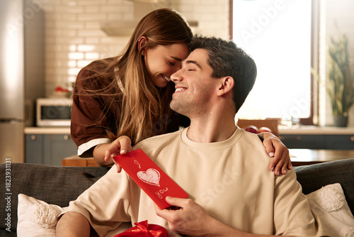 Happy couple celebrating Valentine's Day at home with card and heart-shaped gift box