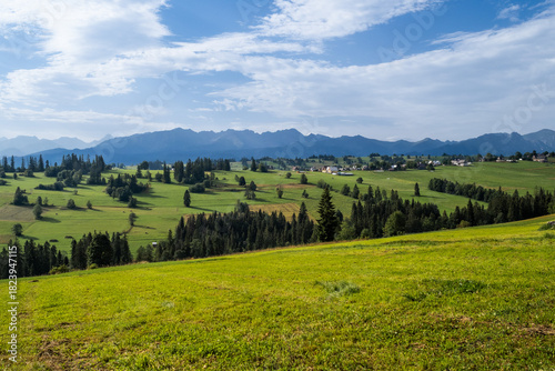 Fototapeta Naklejka Na Ścianę i Meble -  Wide aerial panorama of Sierockie village in the Podhale region, Poland. Lush green farmlands and rolling hills with the majestic Tatra Mountains in the distance.