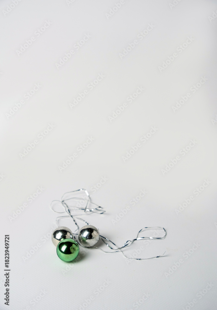 Obraz premium Green and silver Christmas tree balls and tinsel on a white background, space for text