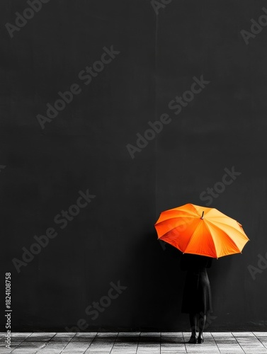 Person standing in front of a black wall, holding an orange umbrella. the person is wearing a black dress and is standing on a tiled floor.