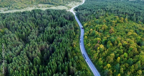 Aerial view of a winding road through dense forest and green countryside