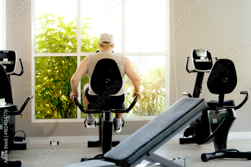 A man in athletic wear works out on an elliptical trainer in a bright and modern gym. His intense expression shows determination and focus as he continues his fitness routine.
