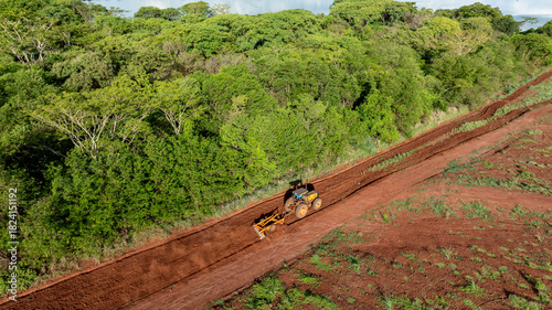 Tractor with agricultural implement plowing land next to riparian forest