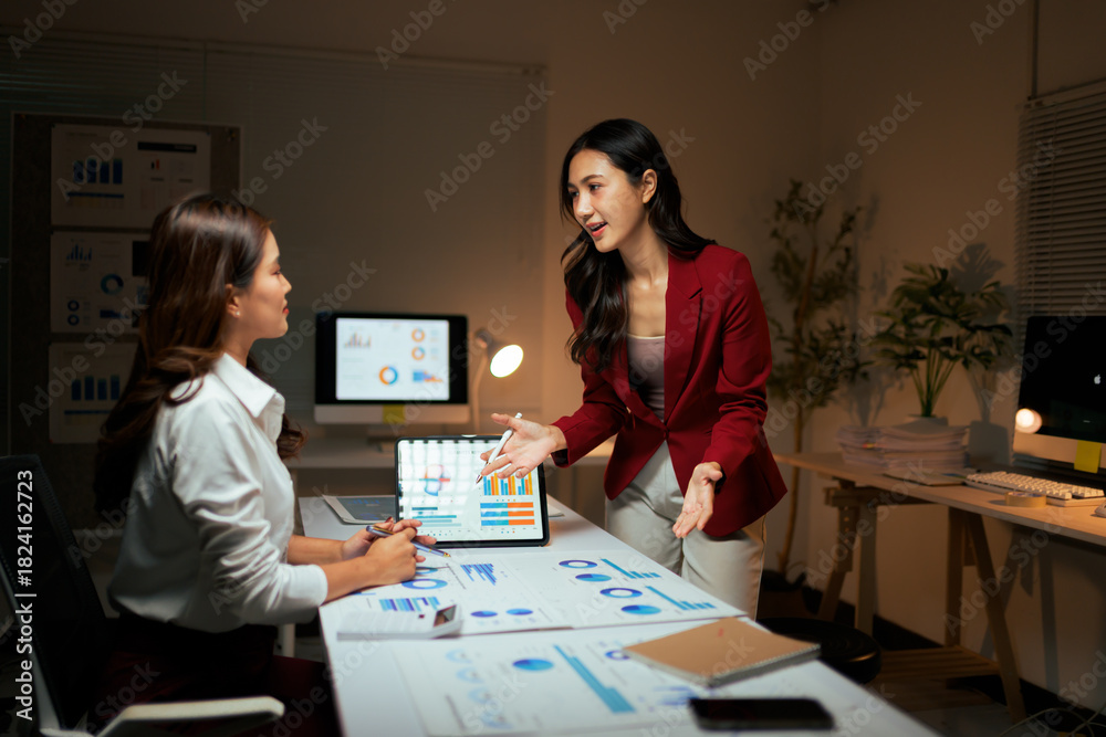 Fototapeta premium Businesswomen discussing data analysis charts late at night