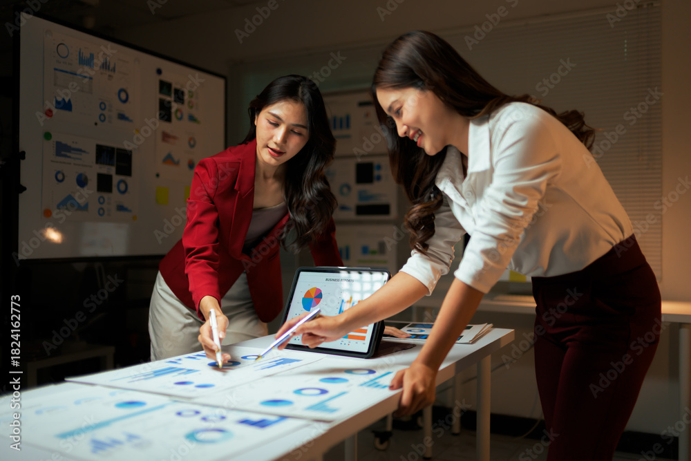 Fototapeta premium Two businesswomen analyzing data charts working overtime in office