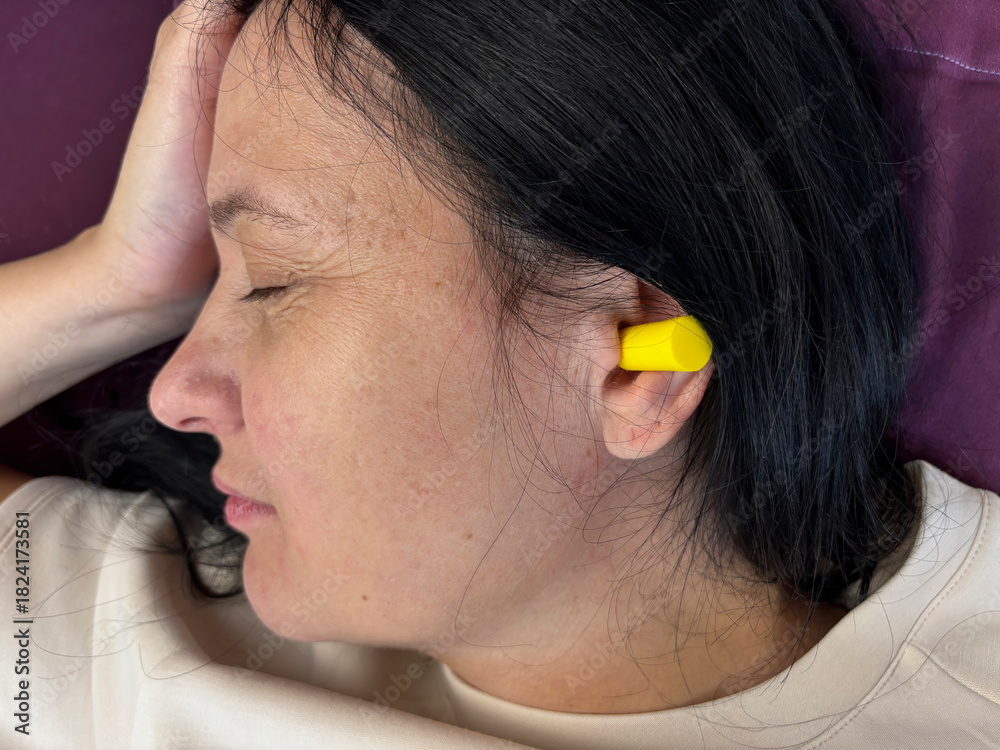 Fototapeta premium Close up of adult brunette woman sleeping with yellow earplugs, noise protection for healthy sleep, deep rest, insomnia prevention and peaceful home bedroom atmosphere