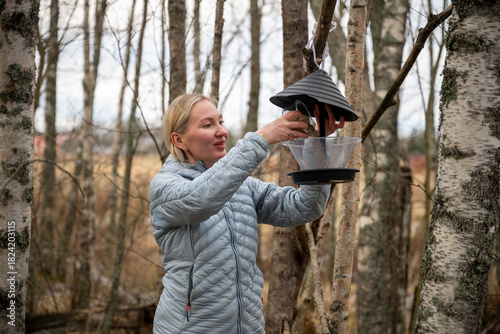 Картината върху платно Woman refilling bird feeder in autumn forest