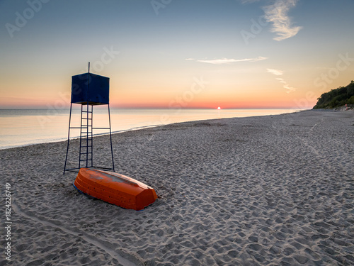 Fototapeta Naklejka Na Ścianę i Meble -  Sunriseat lifeguard hut and boat on beach by Sea