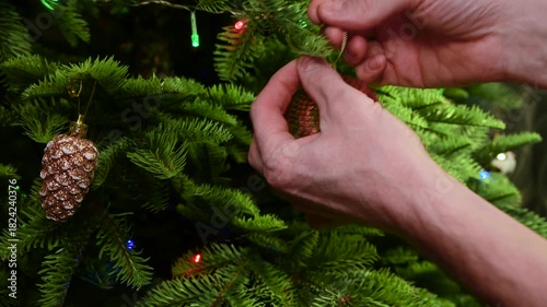 Decorating an artificial Christmas tree. A man hangs a glittering ball on a branch. Celebrating the New Year.